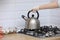 Woman puts a kettle on the kitchen in gloves on gas stove. Stovetop whistling kettle in hand. selective focus