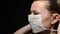 Woman puts on medical mask on black background
