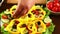 A woman puts pieces of black olives in a plate with a vegetable salad. Close-up.