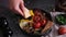 woman puts tasty dish breakfast onto dark background - fried bacon, eggs, mushrooms and tomatoes in ceramic pot