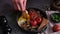 woman puts tasty dish breakfast onto dark background - fried bacon, eggs, mushrooms and tomatoes in ceramic pot