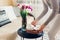 Woman puts tea kettle and cup on rattan tray on coffee table. Interior and home decor. Fresh tulips flowers put in vase
