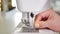 Woman puts thread in needle in sewing machine preparing to work, hands closeup.