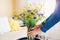 Woman puts vase with blue and yellow flowers on table. Taking care of coziness at home. Interior with Ukrainian colors