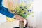 Woman puts vase with blue and yellow flowers on table. Taking care of coziness at home. Interior with Ukrainian colors