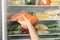 Woman putting bag with carrot in refrigerator with frozen vegetables, closeup