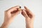 Woman putting battery into hearing aid on light background