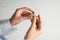 Woman putting battery into hearing aid on light background