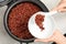 Woman putting brown rice into bowl from multi cooker on grey background