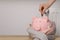 Woman putting coin into piggy bank near heating radiator, closeup. Space for text