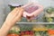 Woman putting container with tomatoes in refrigerator with frozen vegetables