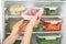 Woman putting container with tomatoes in refrigerator with frozen vegetables