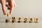 Woman putting cube with letter onto stacked coins to make word Import on light grey table, closeup