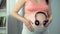 Woman putting earphones on her pregnant belly, enjoying favorite music with baby