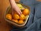 A woman putting her hand into a basket of fruit and pulling out an orange