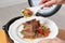 Woman putting meat and garnish prepared in multi cooker on plate