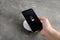 Woman putting mobile phone onto wireless charger at  grey table, closeup