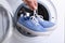 Woman putting pair of sport shoes into washing machine, closeup