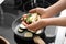 Woman putting sliced zucchini onto frying pan in kitchen