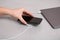 Woman putting smartphone on wireless charger connected to laptop at light grey table, closeup. Space for text