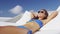Woman putting on sunglasses lying down in sunbed wearing bikini