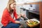 Woman Putting Tray Of Roast Vegetables Into Oven