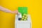 Woman putting used foil container into trash bin on color background, closeup