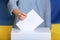 Woman putting voting paper into ballot box against Ukrainian flag,