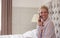 Woman In Pyjamas Sitting On Bed Making Call On Mobile Phone