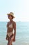 Woman radiates summer vibes wearing yellow striped bikini and a straw hat, enjoying her time on the beach