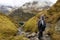 A woman in a rain cape descends a mountain path overlooking fog and a mountain lake. Austria, Alps