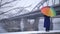 Woman with rainbow umbrella near bridge in winter