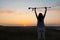 Woman raising hands with elbow crutch up to sky outdoors at sunrise, back view. Healing miracle