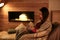 Woman reading book near decorative fireplace at home.