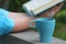 Woman reading book outdoors, coffee cup