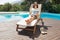 Woman reading book on sun lounger by pool