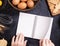 Woman is reading cookbook recipe of making Halloween cookies with baking ingredients, design concept of cooking class, top view,