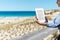 Woman Reading E-Reader At Fence On Beach