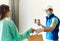 Woman receiving packages from delivery man. Courier in uniform face mask gloves holding paper boxes for take out food