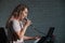 A woman records a vocal lesson using a laptop and accompanying on a keyboard while at home. The teacher sings a song