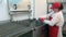 Woman in red apron and cap washes industrial deep fryer in workshop.