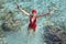 Woman in a red bathing suit standing in the sea and gives to us hands