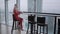 Woman in red coral business suit drinks coffee at a high table near the window. Young blonde businesswoman in the office