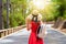Woman in red dress and hat stand on the road with a backpack. forest on a sunny day.