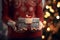 A woman in a red dress holds a gift box in her hands on the background of a Christmas tree 1
