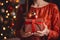 A woman in a red dress holds a gift box in her hands on the background of a Christmas tree