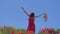 Woman in red dress raised her hands up on Poppy Flowers Field at summer, blue sky