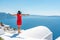 Woman in red dress on the roof enjoying view of Santorini island and Caldera in Aegean sea.