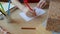 Woman in red dress sits at the wooden table, takes a red felt pen and makes greeting card