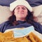 Woman with red hair lies in bed sick with coronavirus with a cold compress on her head
